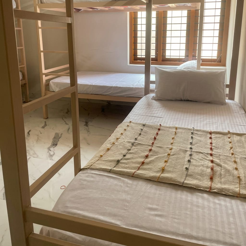 Lower bunk in the ZENWAYS dorm made up with white linen and a handwoven cotton throw