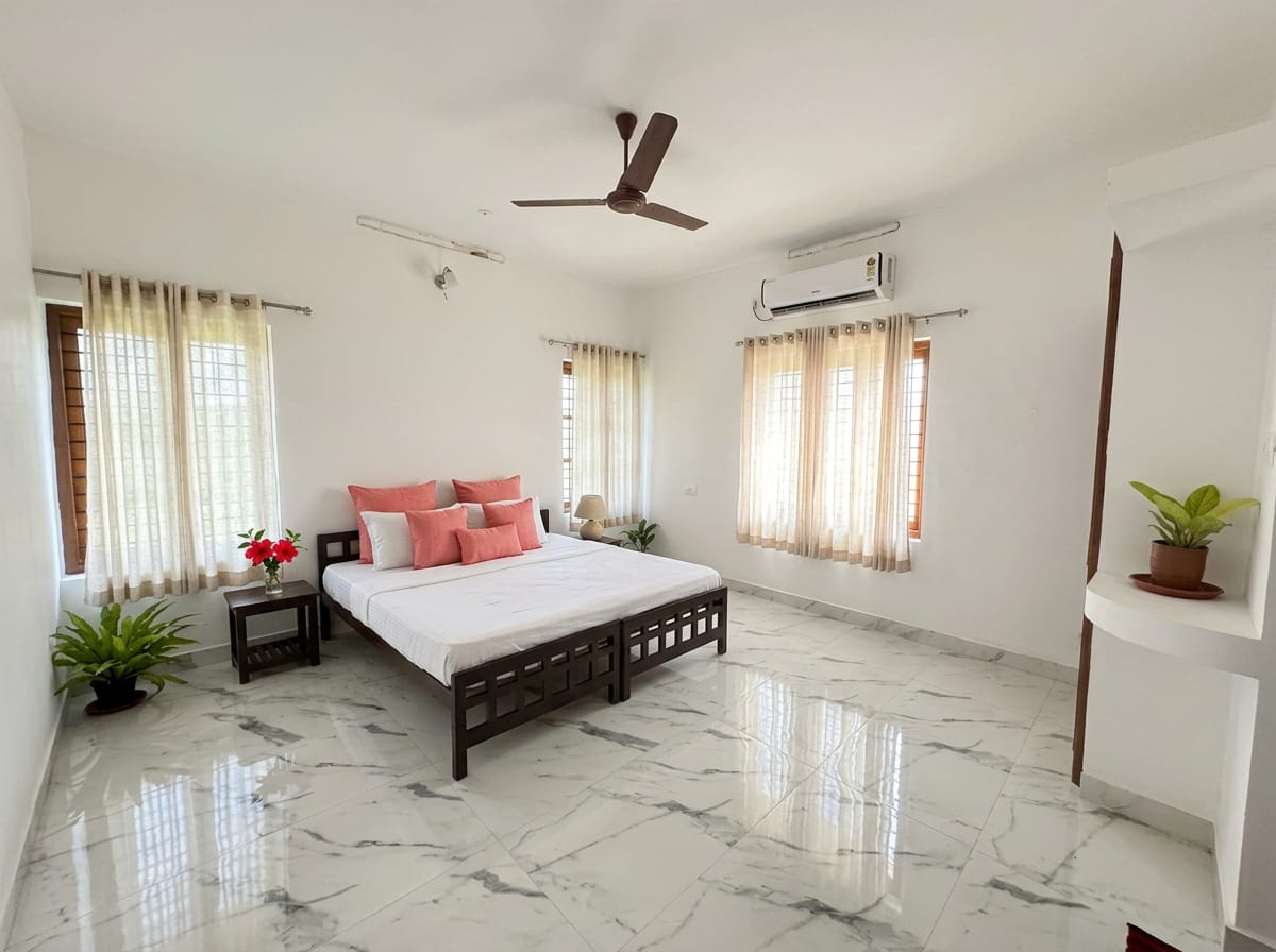 The Hibiscus Room — crisp white bed, cane armchair and a vase of red hibiscus on the bedside table